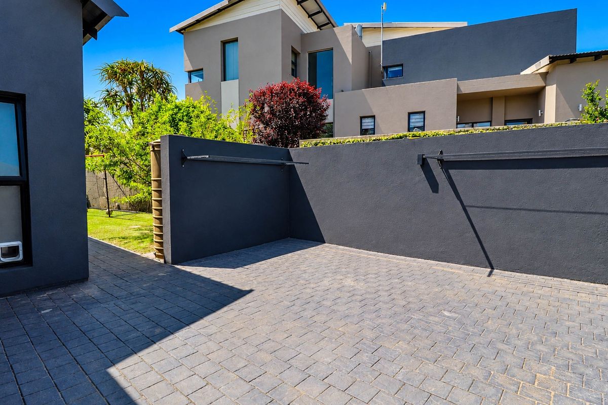 A private paved rear courtyard area featuring a modern boundary wall and integrated wall-mounted drying racks, set against the rear elevation of the house.
