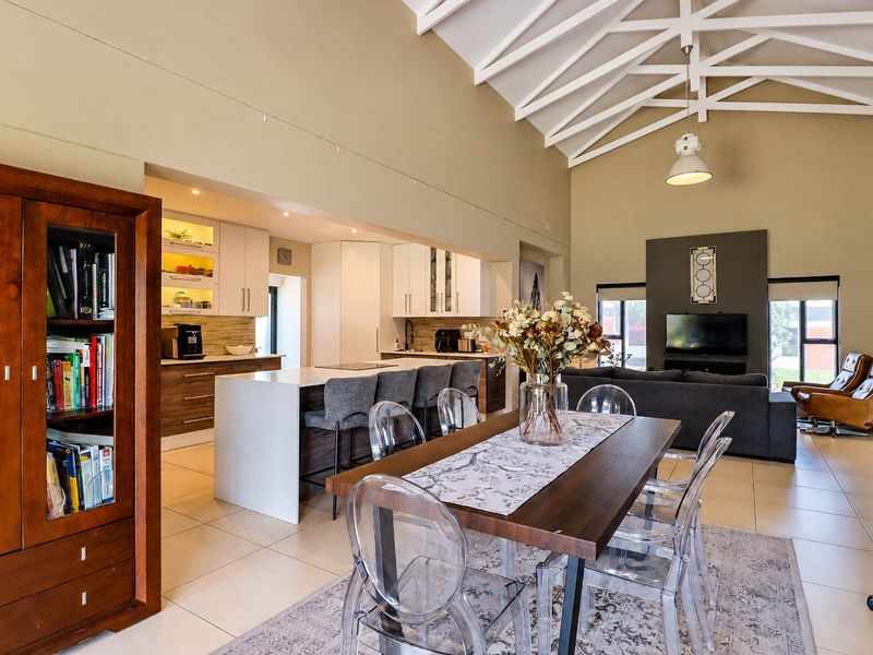 Spacious open-plan living area featuring a modern kitchen with island, dining space, and high vaulted ceilings with exposed white trusses.