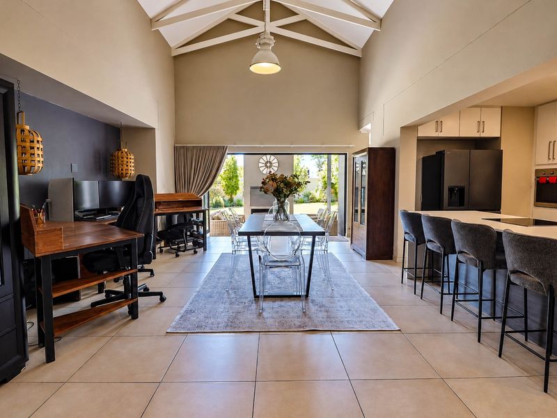 Spacious open-plan living area featuring a vaulted ceiling with exposed rafters, a modern kitchen with island, and seamless flow to the outdoor patio.