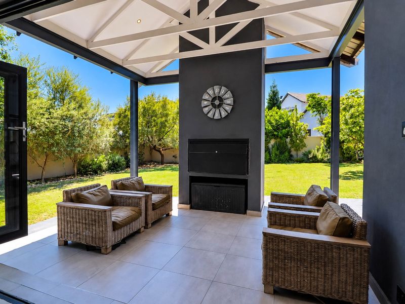 A modern covered patio featuring a built-in fireplace, tiled flooring, and exposed roof trusses, seamlessly connecting to the garden through bi-fold doors.