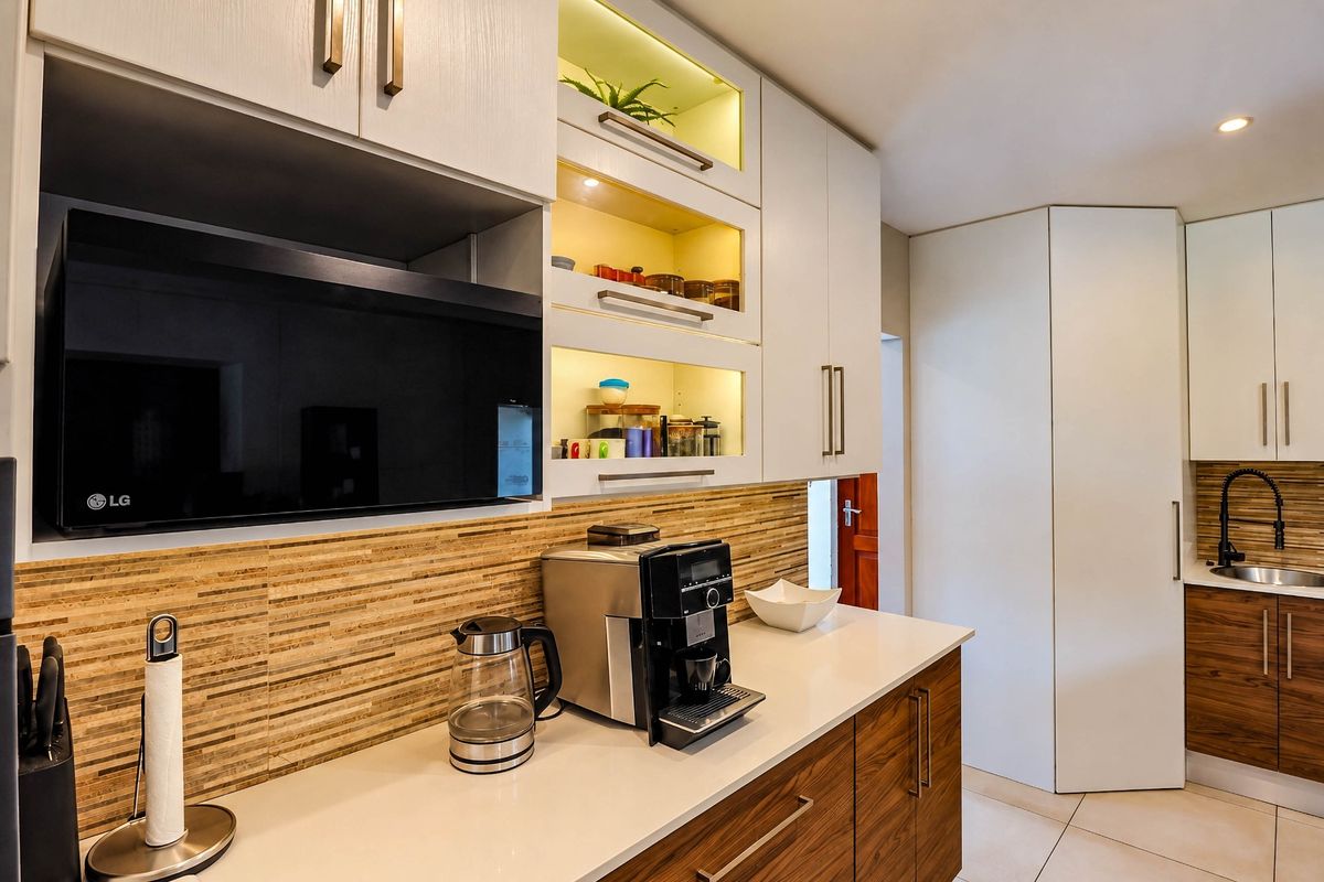 Modern kitchen featuring sleek two-tone cabinetry, quartz countertops, integrated microwave, and stylish tiled backsplash with warm under-cabinet lighting.
