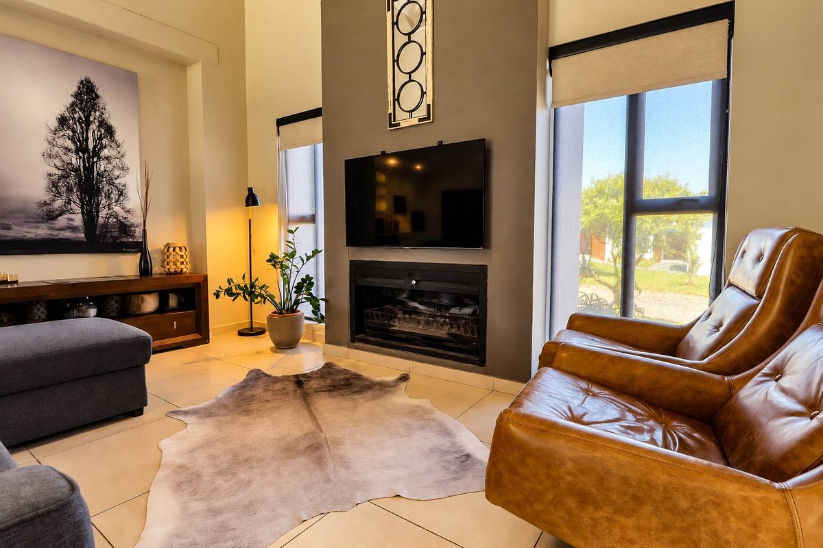 Modern living room featuring a central built-in fireplace, large windows with roller blinds, and neutral tiled flooring, creating a bright and comfortable atmosphere.