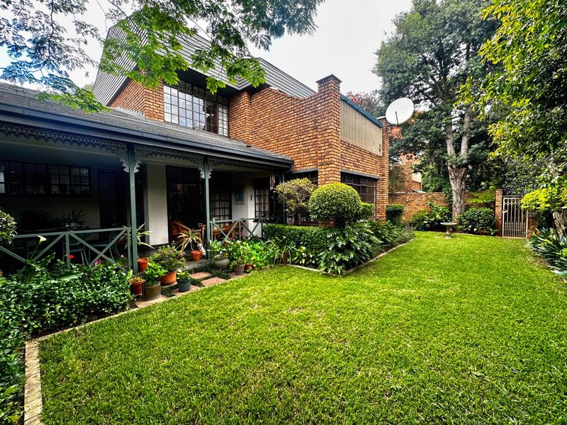 Rear view of a double-story brick townhouse featuring a covered patio, established garden, and classic architectural detailing.