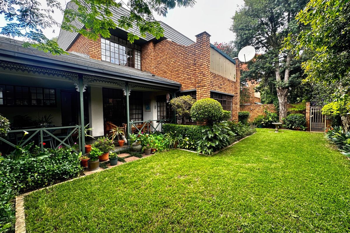 Rear view of a double-story brick townhouse featuring a covered patio, established garden, and classic architectural detailing.