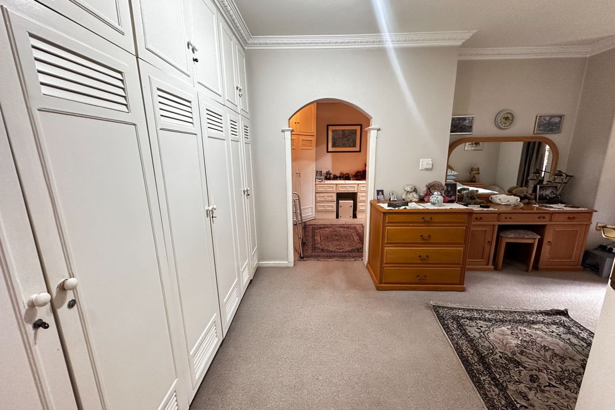 Spacious bedroom featuring extensive built-in cabinetry, decorative crown molding, and an arched entryway leading to an adjoining dressing or vanity area.