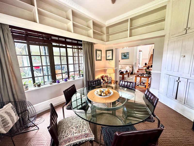 Dining room featuring built-in cabinetry, crown molding, and large multi-pane windows, with an open flow into the adjacent living area.