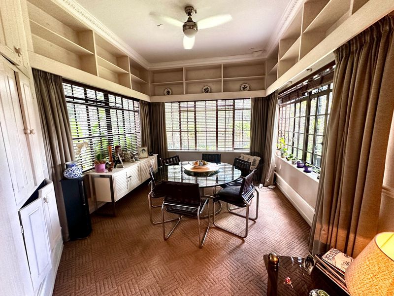 A bright dining room featuring extensive built-in shelving, crown molding, a ceiling fan, and large windows providing ample natural light.