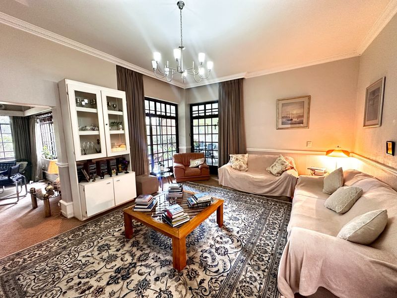 Spacious living room featuring crown molding, wainscoting, a built-in display cabinet, and large multi-pane glass doors providing natural light and garden access.