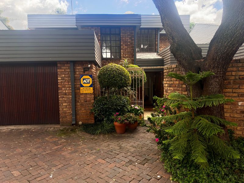 Front elevation of a townhouse featuring a brick facade, paved driveway, and integrated garage entrance with established garden landscaping.