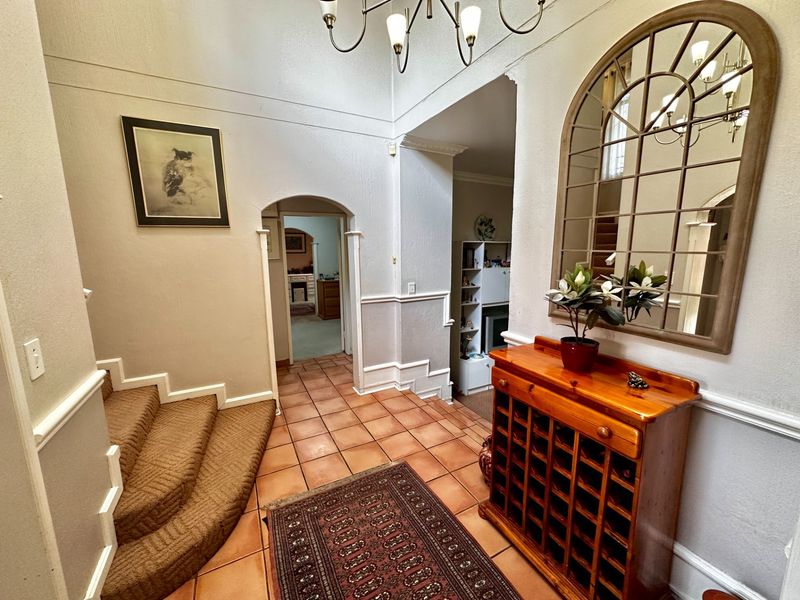 Welcoming entrance hall featuring terracotta floor tiles, a carpeted staircase, and classic architectural archways leading to the living areas.