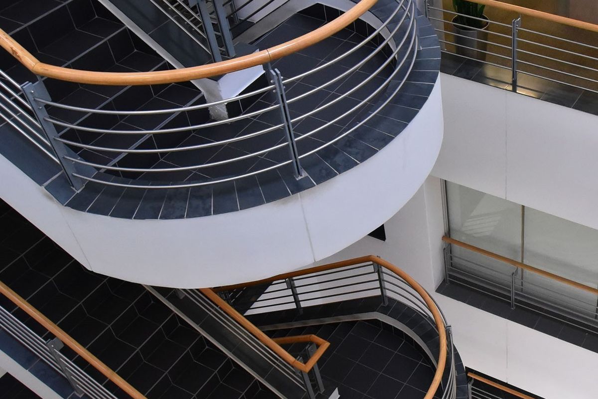 A modern commercial atrium featuring a striking curved staircase with tiled treads, metal balustrades, and wooden handrails.