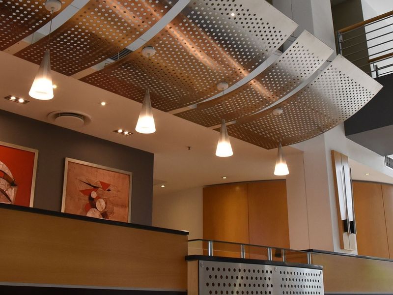 Modern commercial lobby entrance featuring architectural perforated metal ceiling panels, warm timber veneer wall finishes, and contemporary pendant lighting.