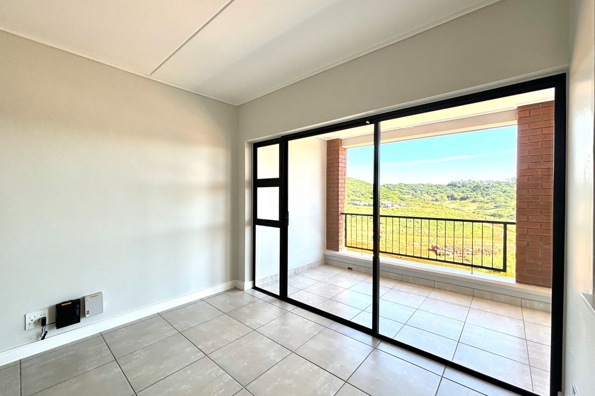 Bright and modern living area featuring large sliding glass doors that open onto a private balcony with scenic hillside views.