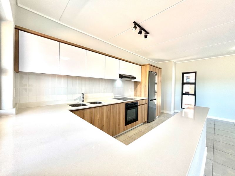 Modern kitchen featuring sleek white and wood-grain cabinetry, quartz countertops, integrated appliances, and a functional breakfast bar layout.