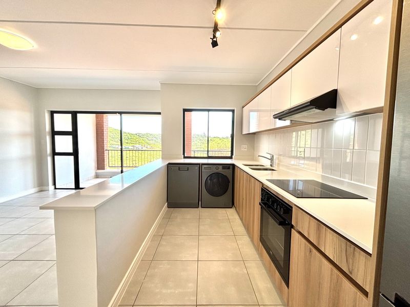Modern open-plan kitchen featuring sleek cabinetry, stone countertops, integrated appliances, and tiled flooring, seamlessly flowing into a bright living area with balcony access.