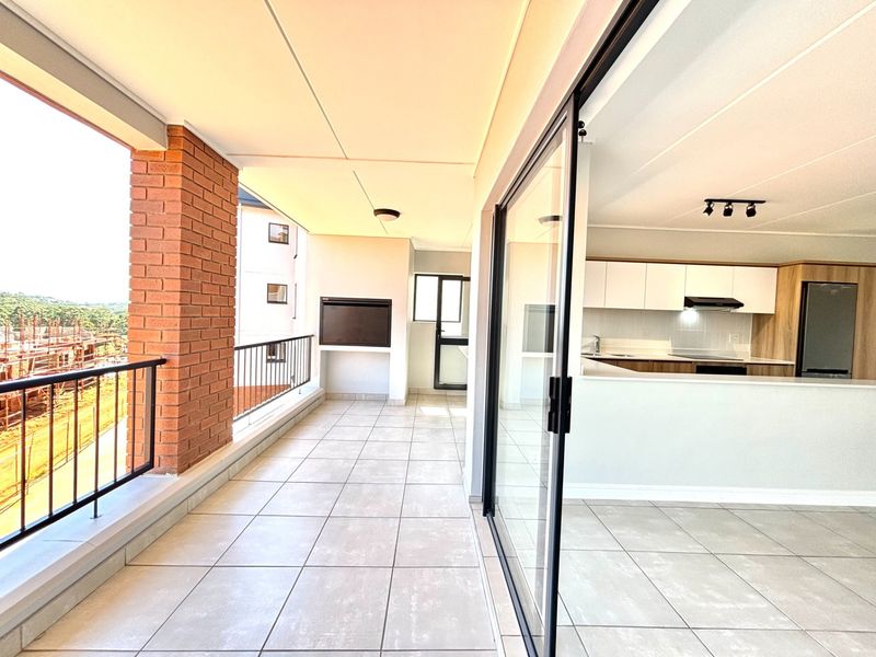 Spacious covered balcony featuring tiled flooring, a built-in braai, and direct access to the open-plan kitchen area through large sliding glass doors.