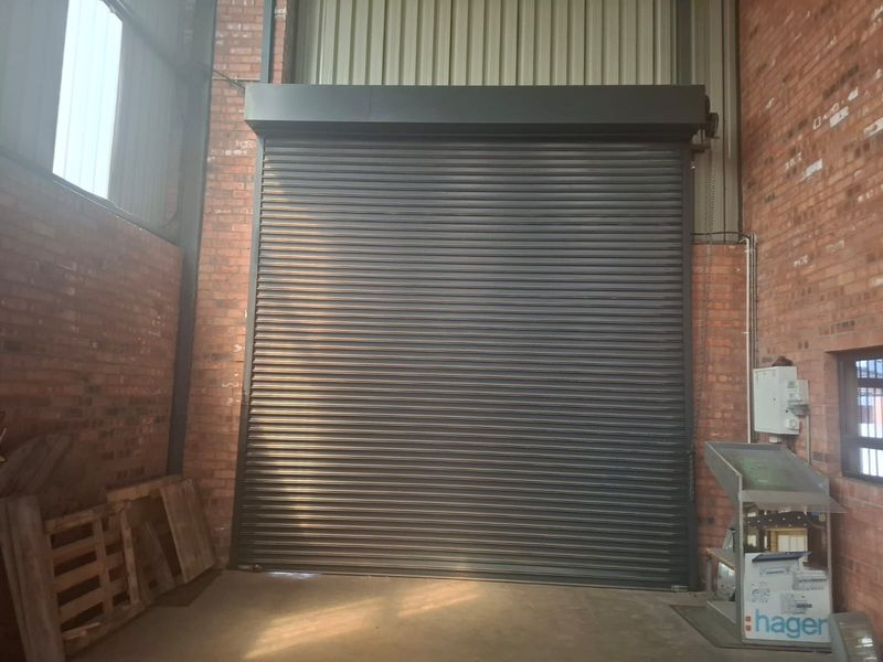 Commercial garage space featuring a large industrial roller shutter door, exposed brickwork, and high ceilings with steel structural elements.