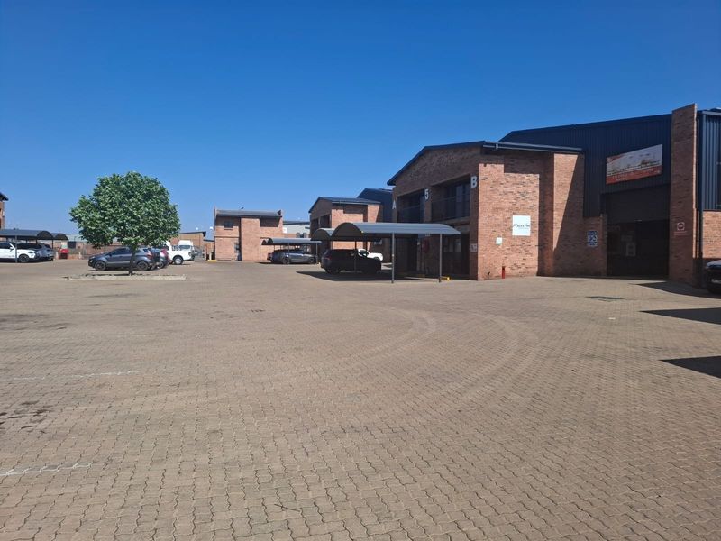 Exterior view of a commercial business park featuring brick buildings, paved parking areas, and covered carports.