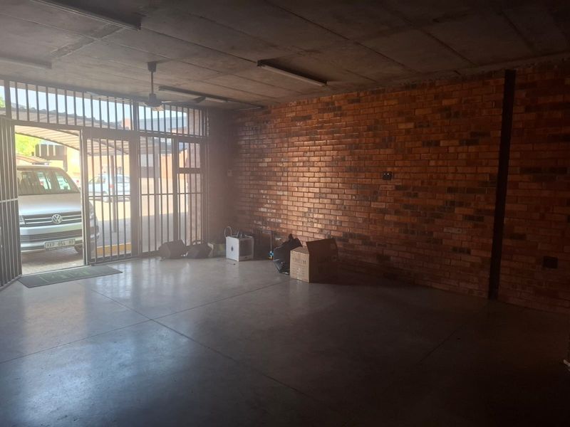 Spacious garage featuring exposed brick walls, concrete flooring, and a secure metal gate entrance, providing ample room for vehicle storage or utility use.