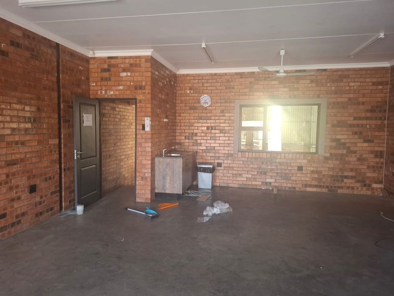 Spacious commercial office area featuring exposed brick walls, concrete flooring, a ceiling fan, and a small kitchenette unit with a sink.
