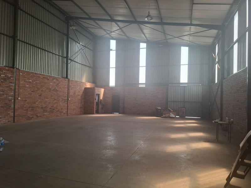 Spacious industrial warehouse unit featuring exposed brick walls, high steel truss ceilings, concrete flooring, and large sliding access doors.