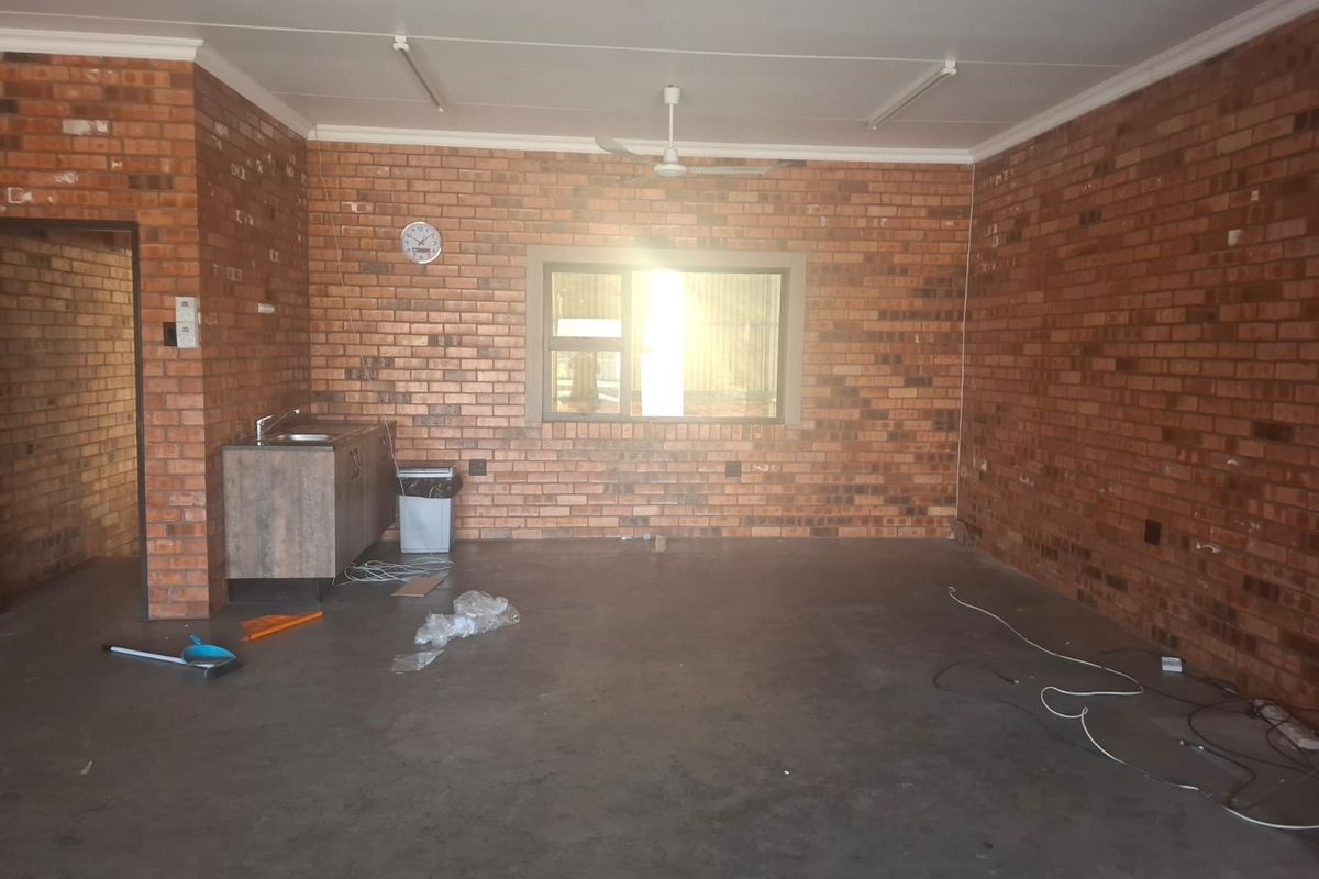 A functional utility space featuring exposed brick walls, concrete flooring, a small kitchenette area with a sink, and overhead lighting.
