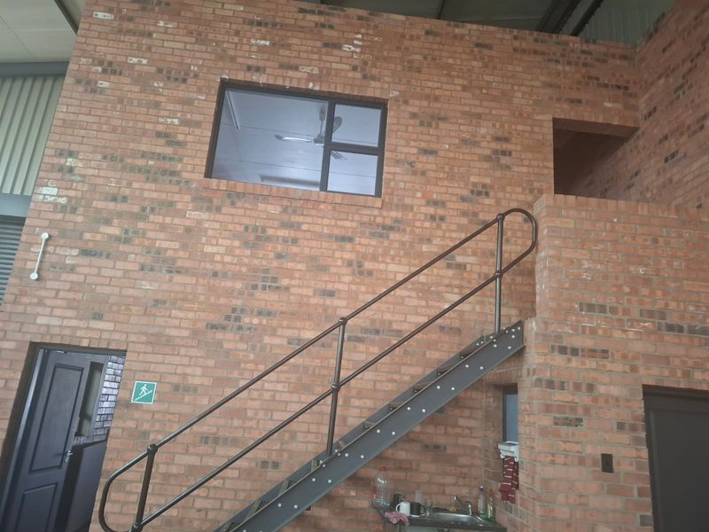 Industrial-style utility space featuring exposed brick walls, a metal staircase with handrails, and a built-in sink area.