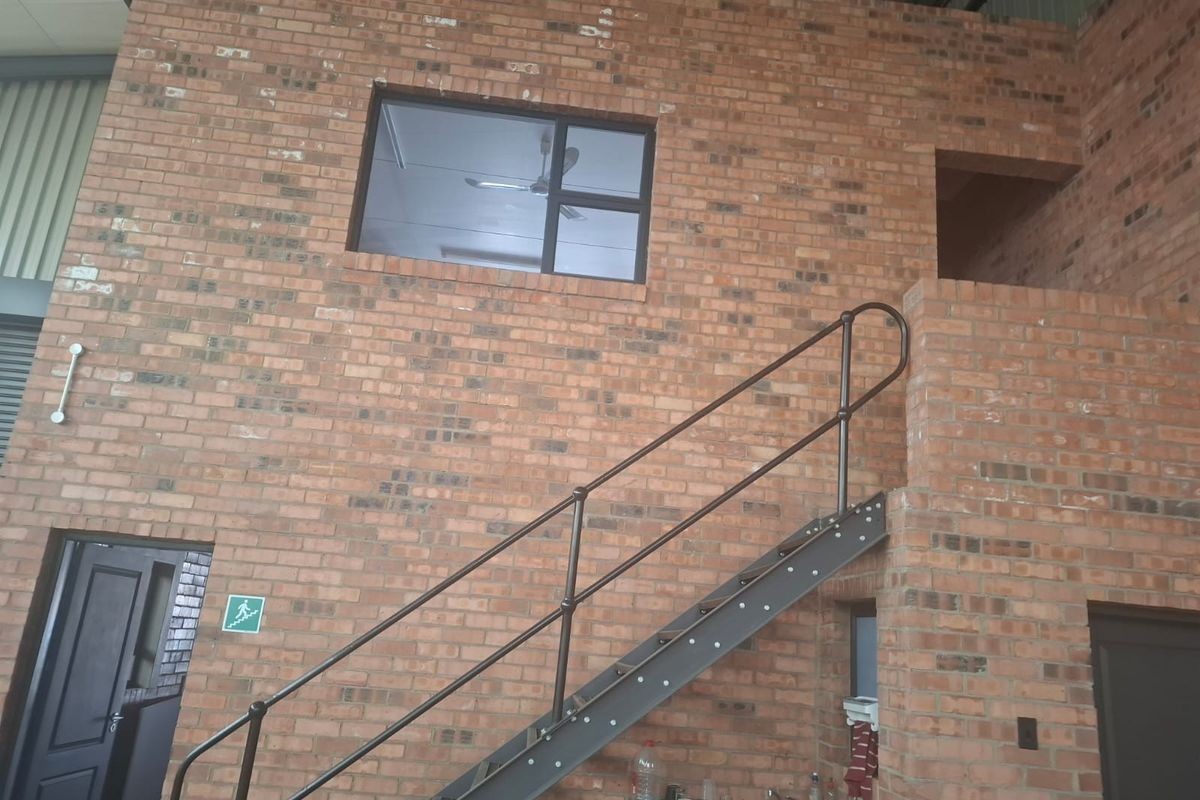 Industrial-style utility space featuring exposed brick walls, a metal staircase with handrails, and a built-in sink area.