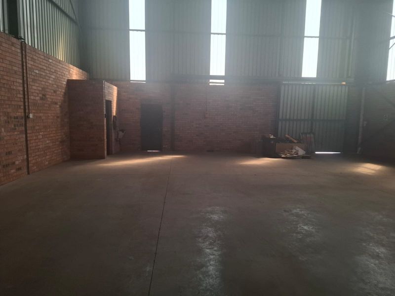 Spacious industrial utility area featuring exposed brick walls, durable concrete flooring, and high ceilings with natural light from translucent roof panels.