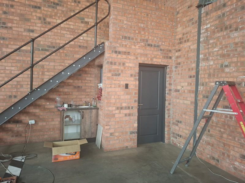 Industrial style utility space featuring exposed brick walls, a metal staircase, and a compact kitchenette area with a sink.