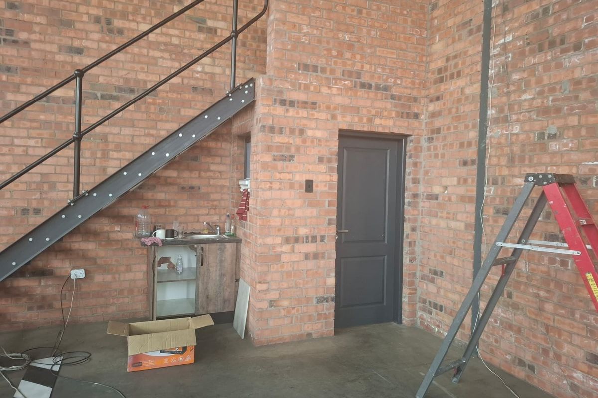 Industrial style utility space featuring exposed brick walls, a metal staircase, and a compact kitchenette area with a sink.