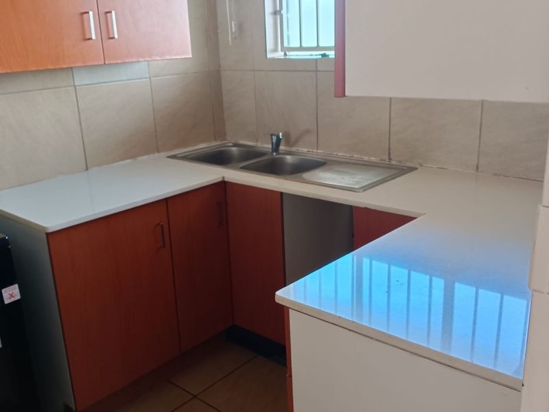 A compact kitchen featuring built-in cabinetry, a double bowl stainless steel sink, and tiled finishes, offering a functional space ready for updates.