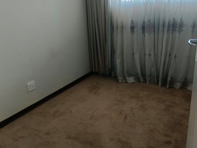 An empty bedroom featuring carpeted flooring and a window with curtains, providing a blank canvas for potential interior design updates.