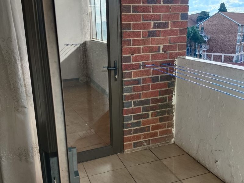 A compact balcony featuring tiled flooring, a brick accent wall, and a glass door entrance, offering an outdoor space for the apartment.