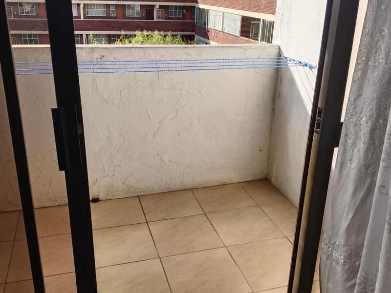 A compact balcony featuring tiled flooring and a sliding door entrance, offering an outdoor space with a view of the surrounding apartment complex.