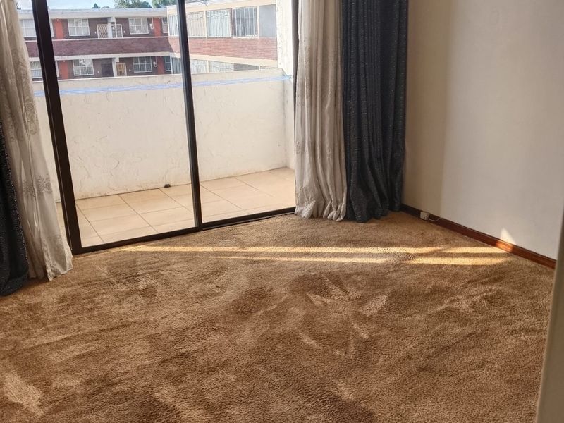 A spacious, empty bedroom featuring carpeted flooring and large sliding glass doors that provide direct access to a private balcony.