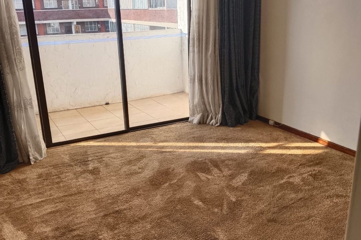 A spacious, empty bedroom featuring carpeted flooring and large sliding glass doors that provide direct access to a private balcony.