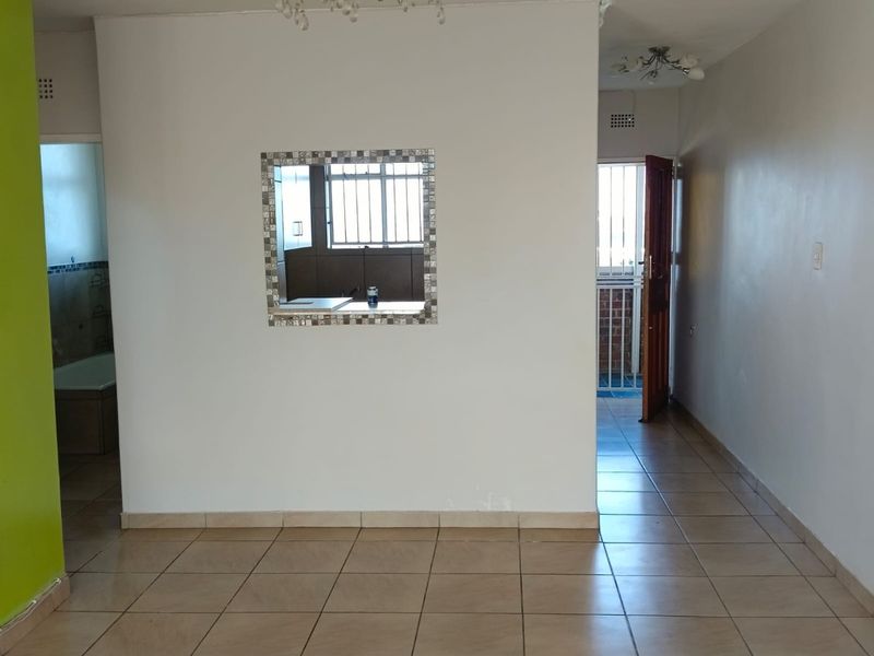 Open plan living area featuring neutral tiled flooring, a decorative pass-through window to the kitchen, and access to an exterior security gate.