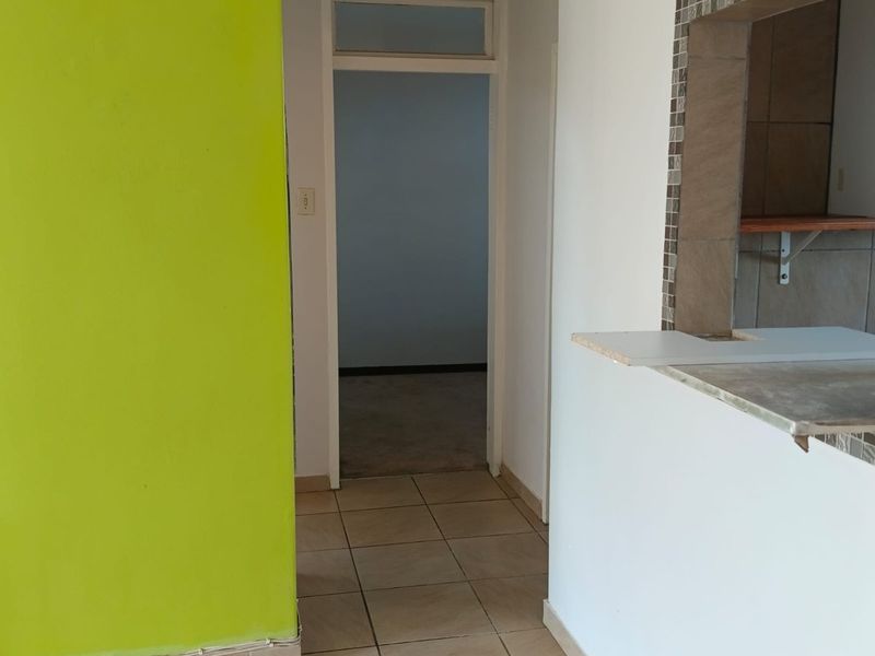A hallway area featuring tiled flooring and a pass-through window connecting to the kitchen, showing signs of wear and unfinished detailing.