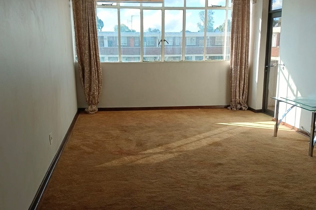 Spacious living area featuring large windows, carpet flooring, and direct access to a balcony, offering a blank canvas for renovation.