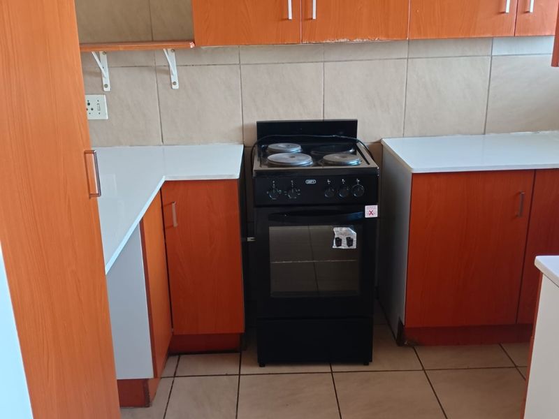 A functional kitchen featuring wood-look cabinetry, white laminate countertops, a tiled backsplash, and a freestanding stove with ceramic tile flooring.