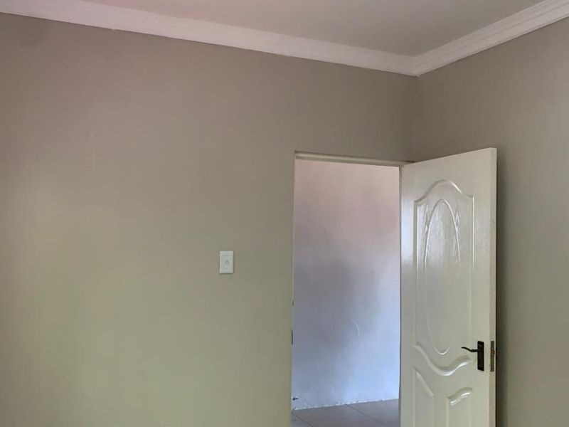 A clean, empty bedroom featuring neutral wall paint, tiled flooring, and a classic moulded panel door.
