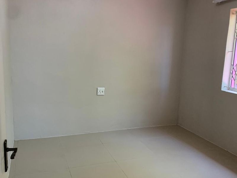 A clean, empty bedroom featuring neutral tiled flooring, cove cornicing, and a window fitted with a security gate.