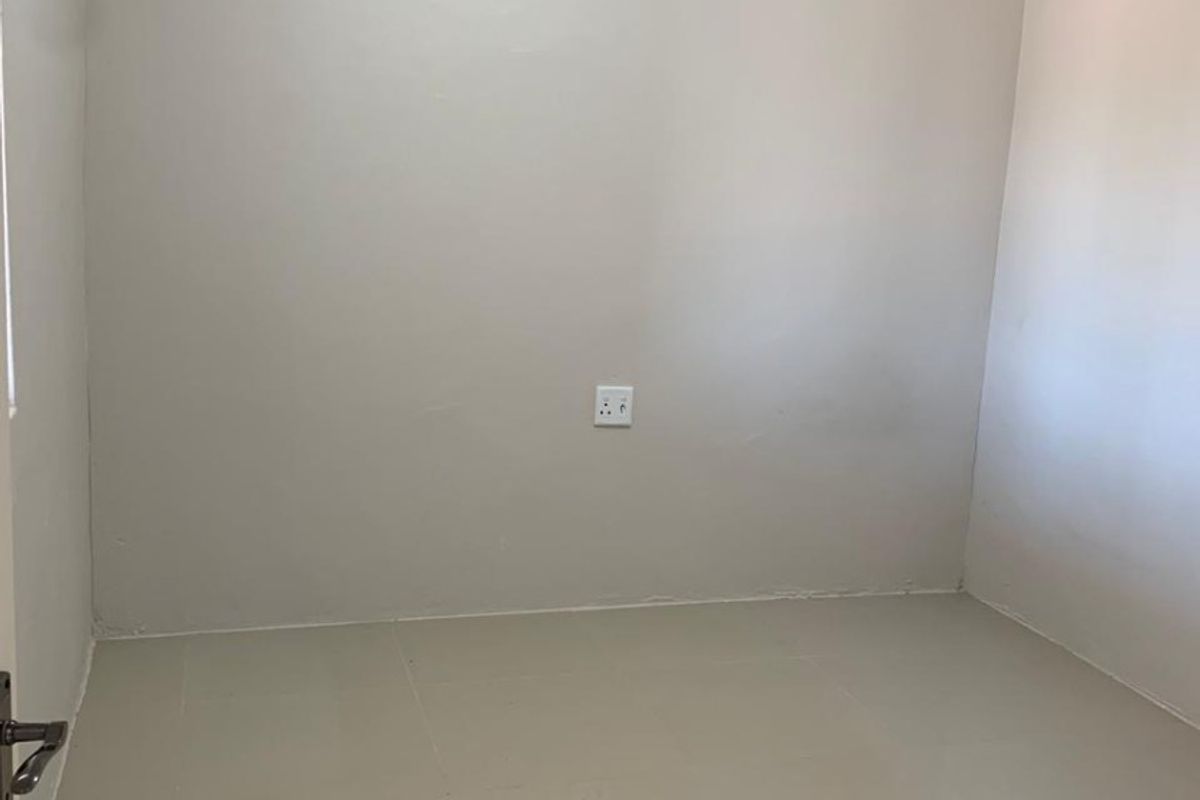 A clean, empty bedroom featuring neutral wall paint, crown molding, and tiled flooring, providing a versatile space ready for personalization.