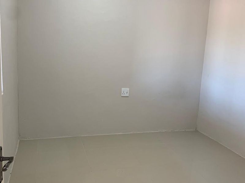 A clean, empty bedroom featuring neutral wall paint, crown molding, and tiled flooring, providing a versatile space ready for personalization.