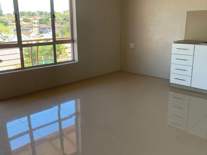 A bright, empty open-plan living area featuring polished tiled floors, neutral walls, and a large window with views, complemented by built-in cabinetry.