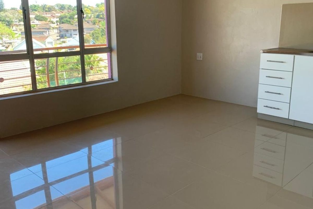 A bright, empty open-plan living area featuring polished tiled floors, neutral walls, and a large window with views, complemented by built-in cabinetry.