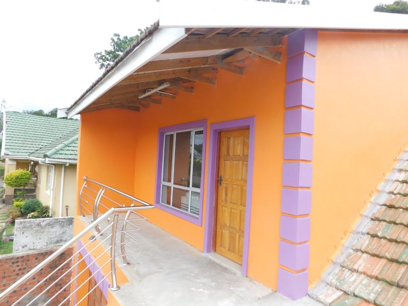 An elevated balcony area featuring a stainless steel balustrade, timber door, and aluminium window frame, with unfinished roof rafters visible.