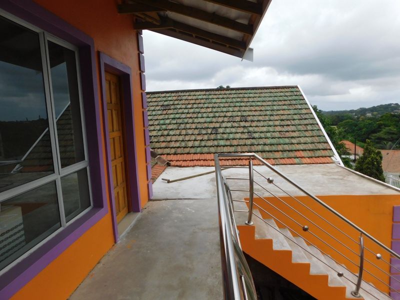 An elevated balcony area featuring a stainless steel balustrade, concrete stairs, and views over the surrounding tiled roof structures.