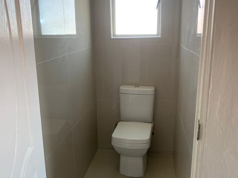 A compact, modern bathroom featuring neutral ceramic wall and floor tiles and a standard white toilet.